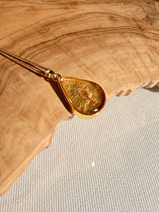 Handgemaakte gouden hanger met iepenzaad op houten ondergrond met warme lichtval