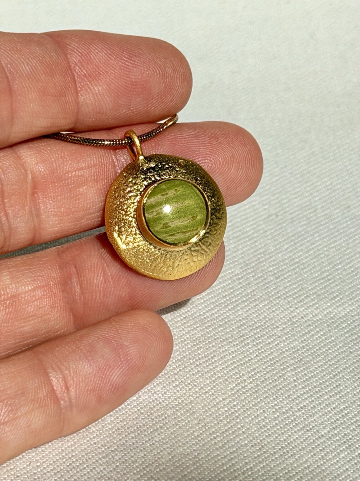 Detail van vergulde hanger met groen varenblad en lichte sporen