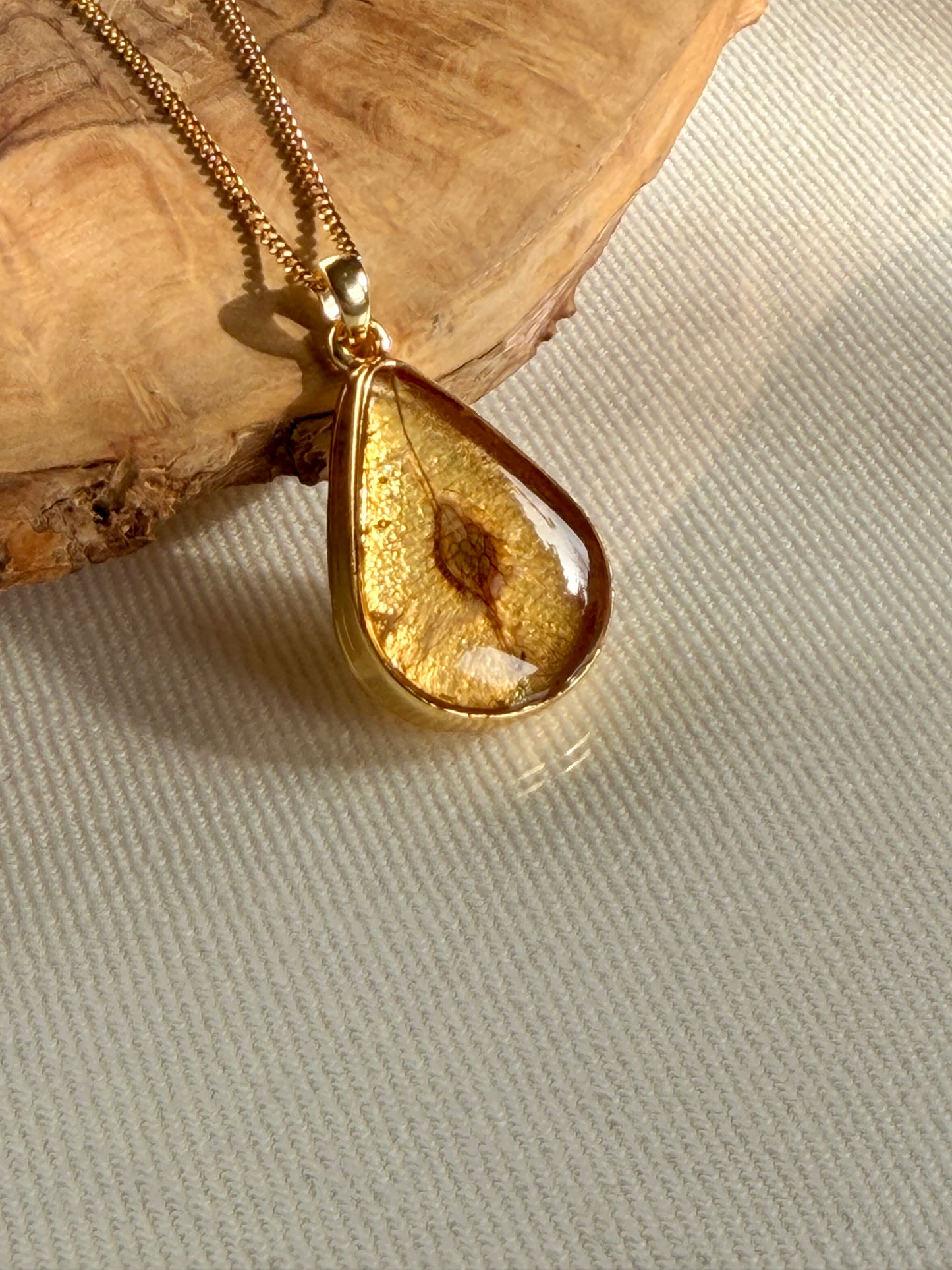 24K vergulde druppelhanger met iepenzaad in resin van BeLeaf Art op lichte stof en hout
