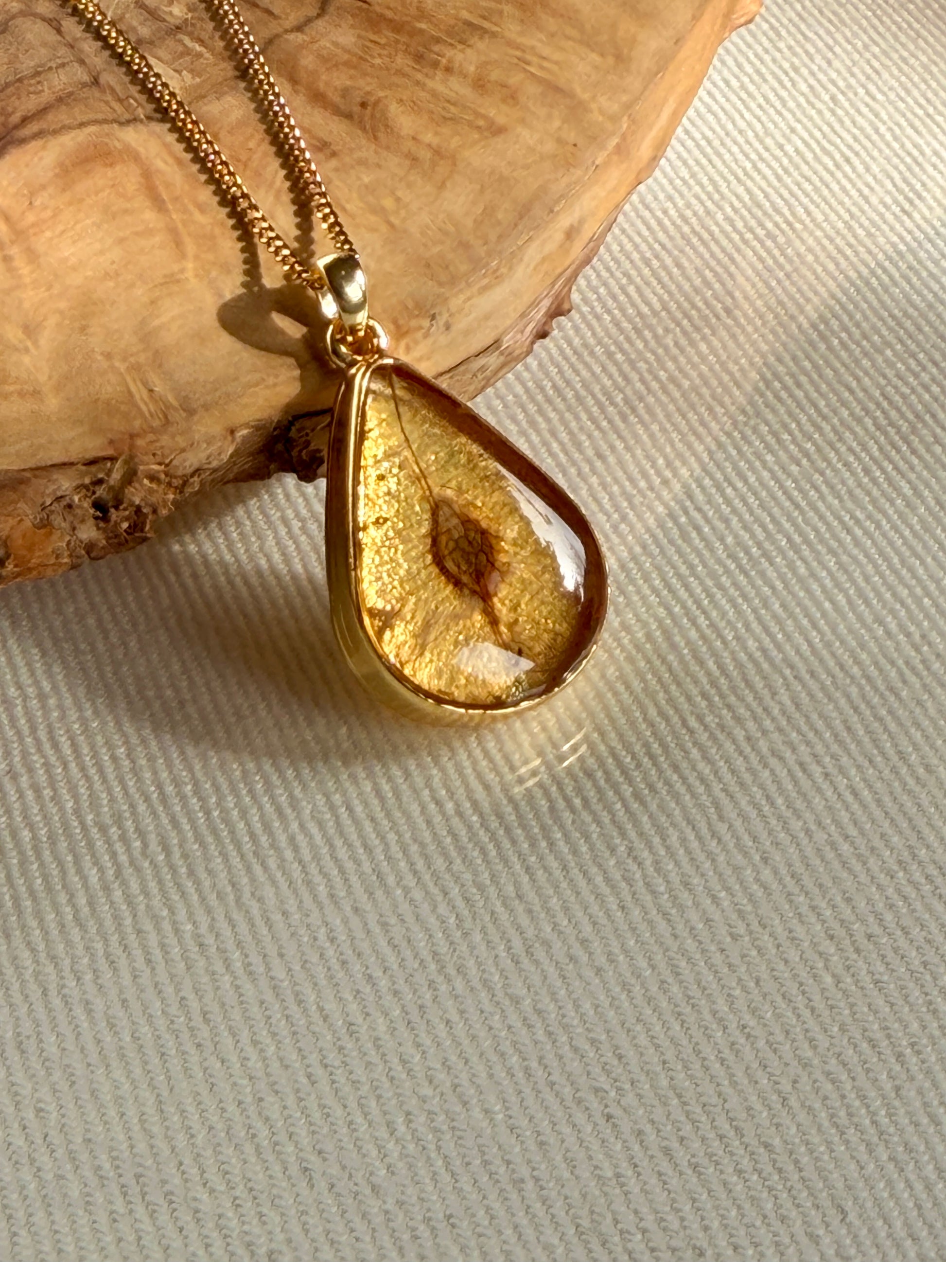 24K vergulde druppelhanger met iepenzaad in resin van BeLeaf Art op lichte stof en hout