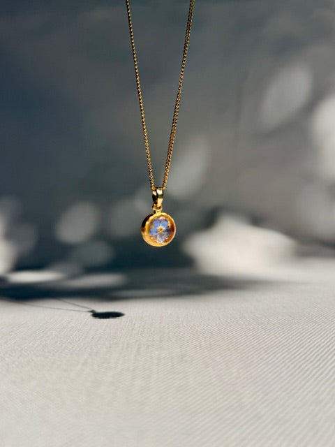 Detail van blauw vergeet-me-nietje in kleine gouden hanger
