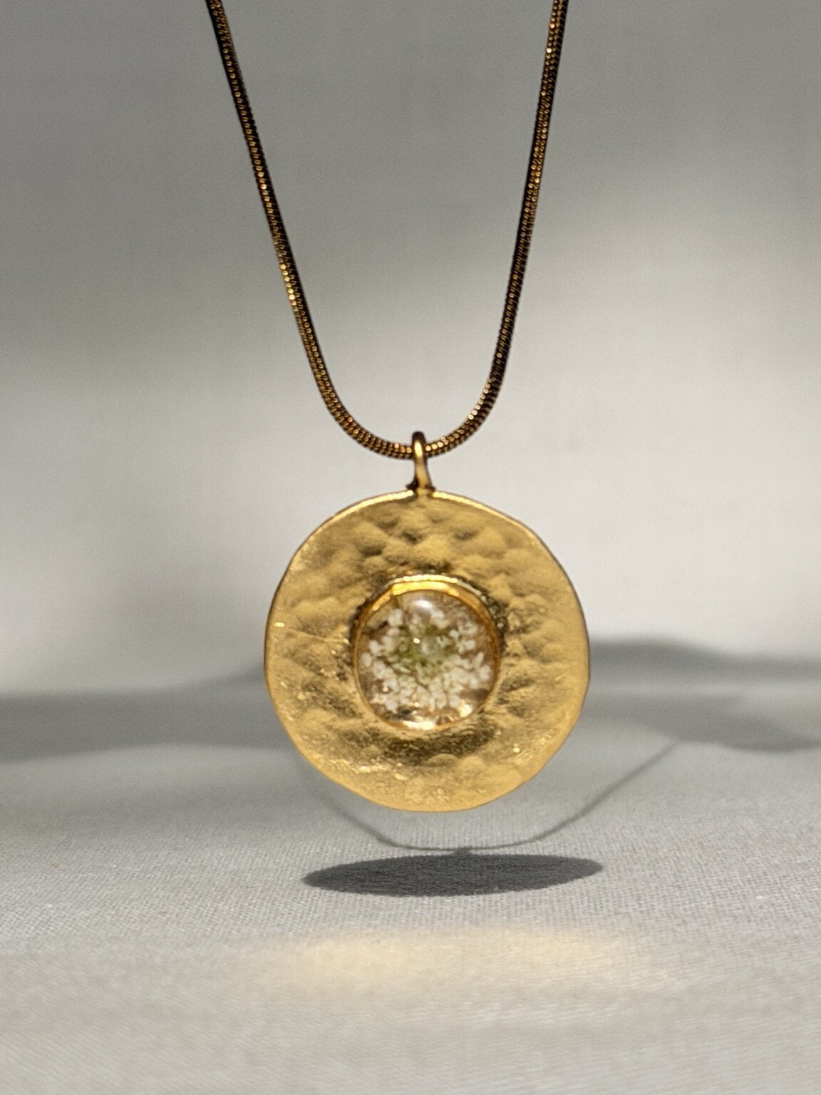 Detail van vergulde hanger met kleine witte schermbloemen in hars