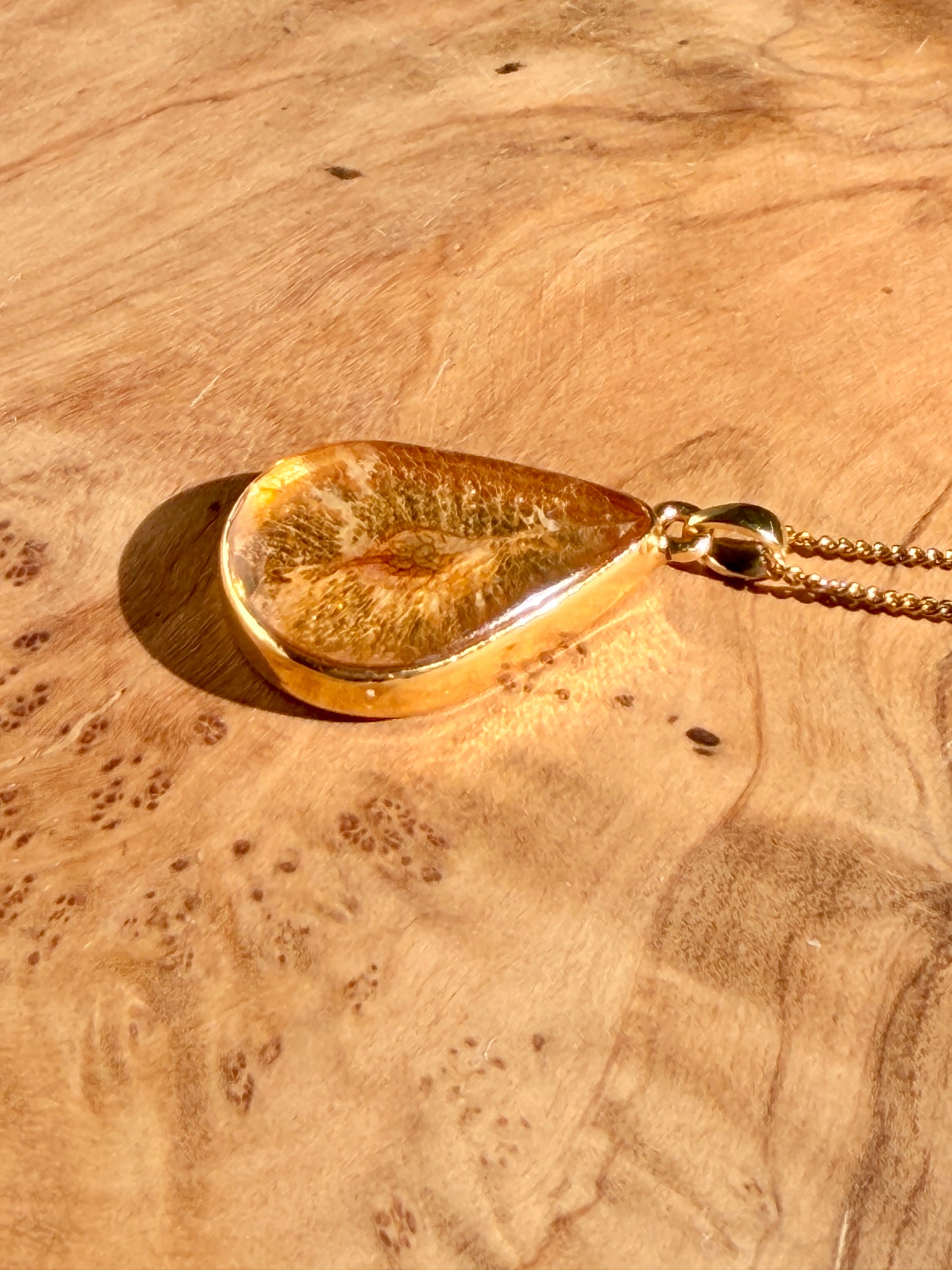 Handgemaakte gouden hanger met iepenzaad op houten ondergrond met warme lichtval