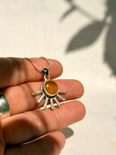 Kleine verzilverde hanger met zonnebloemdetail getoond in de hand voor schaalweergave