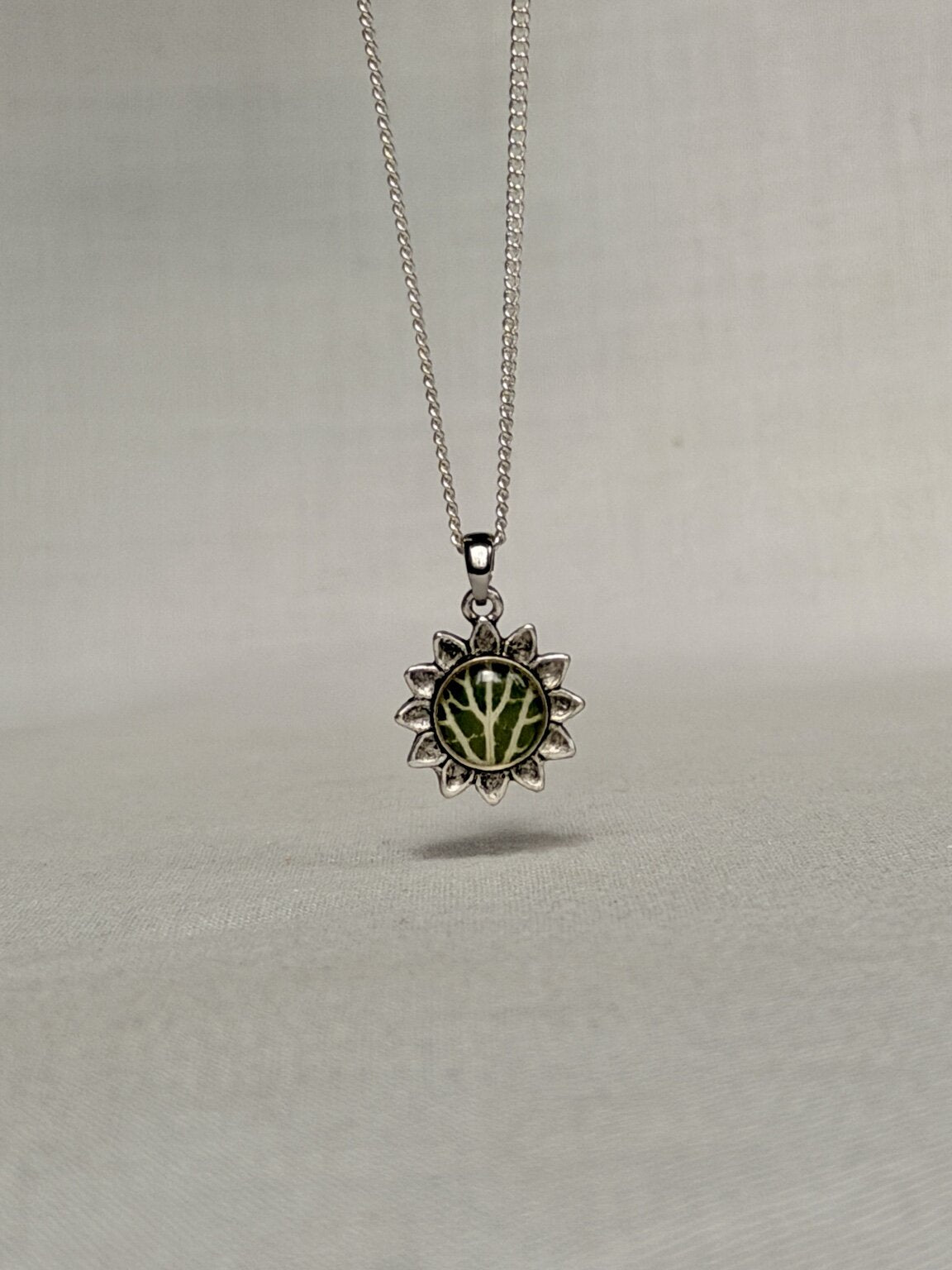 Bloemvormige hanger met groen Fittonia-blad aan een zilveren snake ketting