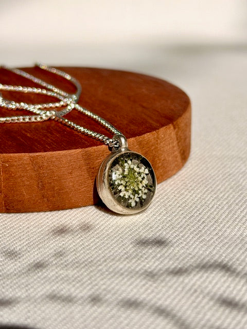 Verzilverde ronde hanger met detail van witte schermbloem en zilveren ketting